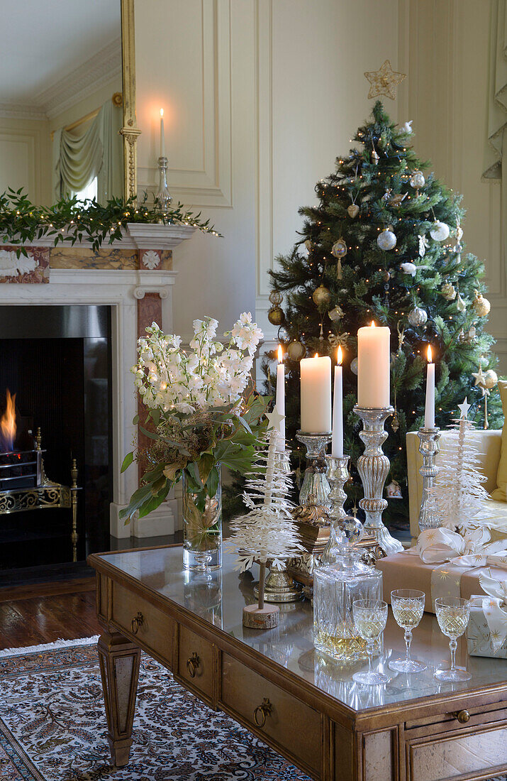Lit candles and decanter with cut flowers with Christmas tree at fireside Kent country house England UK