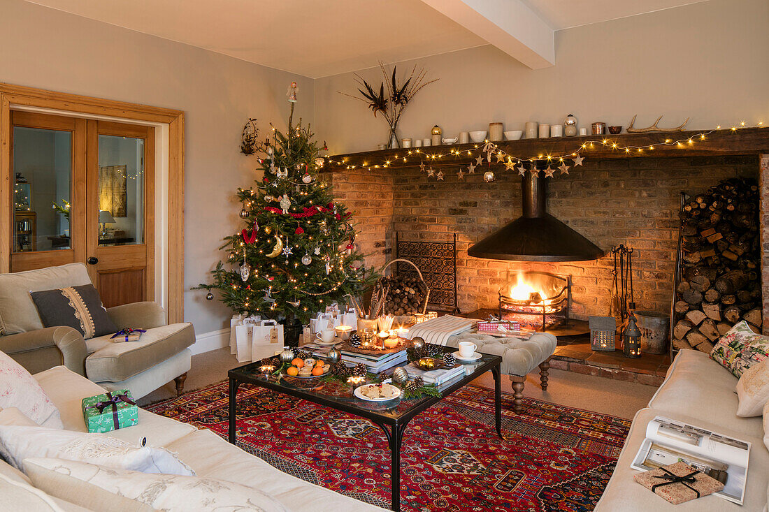 Beleuchteter Baum und Feuer mit Weihnachtsgeschenken im Wohnzimmer in Cheshire, Großbritannien