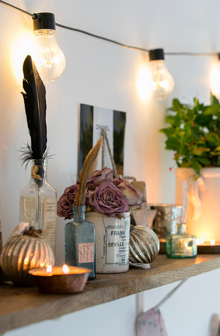 Cut roses and feathers with tealights and lightbulbs in bedroom shelf in Cheshire home UK