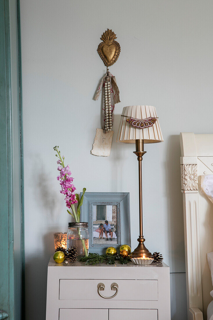 Cremelampe mit Messingherz und einstieliger Blume auf dem Nachttisch in einem Haus in Cheshire, UK