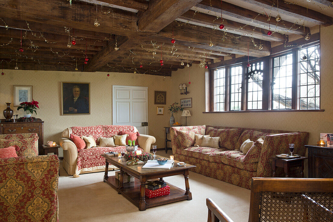 Decorations on ceiling beams above sofas in living room of Hampshire farmhouse England UK