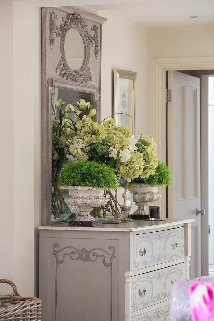 Cut flowers and houseplants on painted chest of drawers in hallway of Sussex country house UK