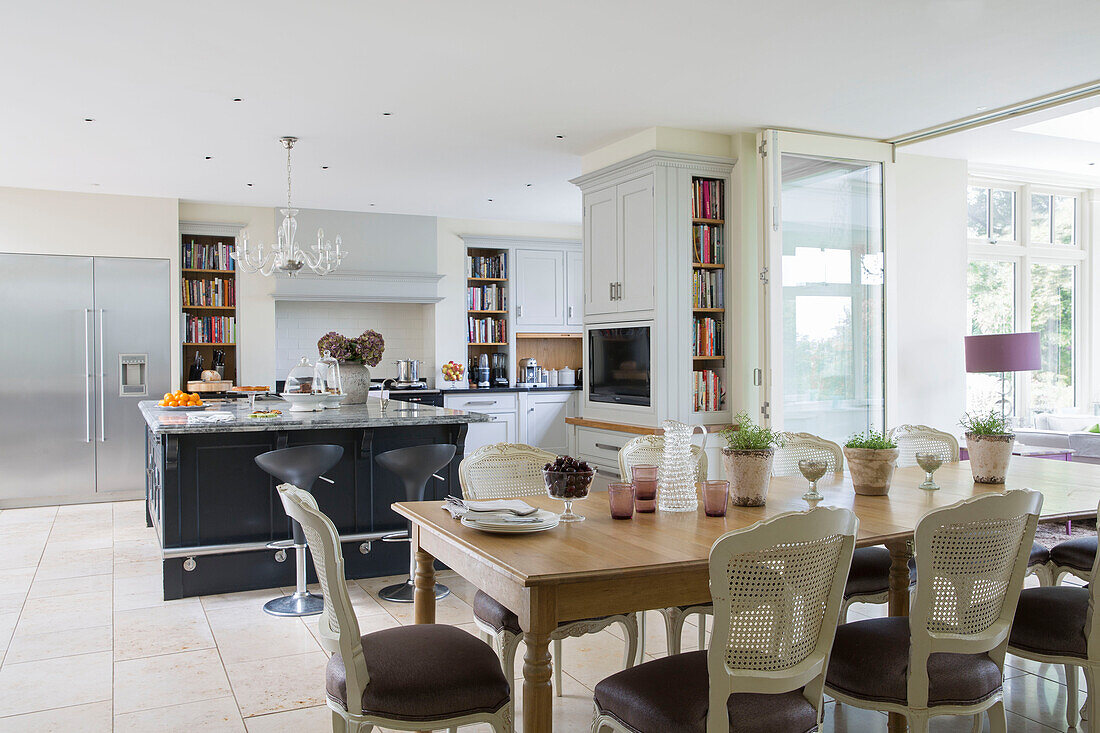 Esszimmerstühle am Holztisch in offener Küche mit Kochinsel und Bücherregalen in einem freistehenden Landhaus in Sussex UK