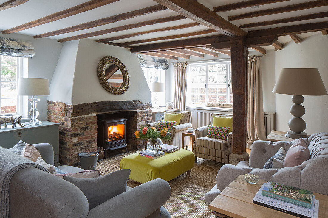 Lampen und graue Sofas mit beleuchtetem Holzofen in einem umgebauten Gasthaus in Kent, Großbritannien