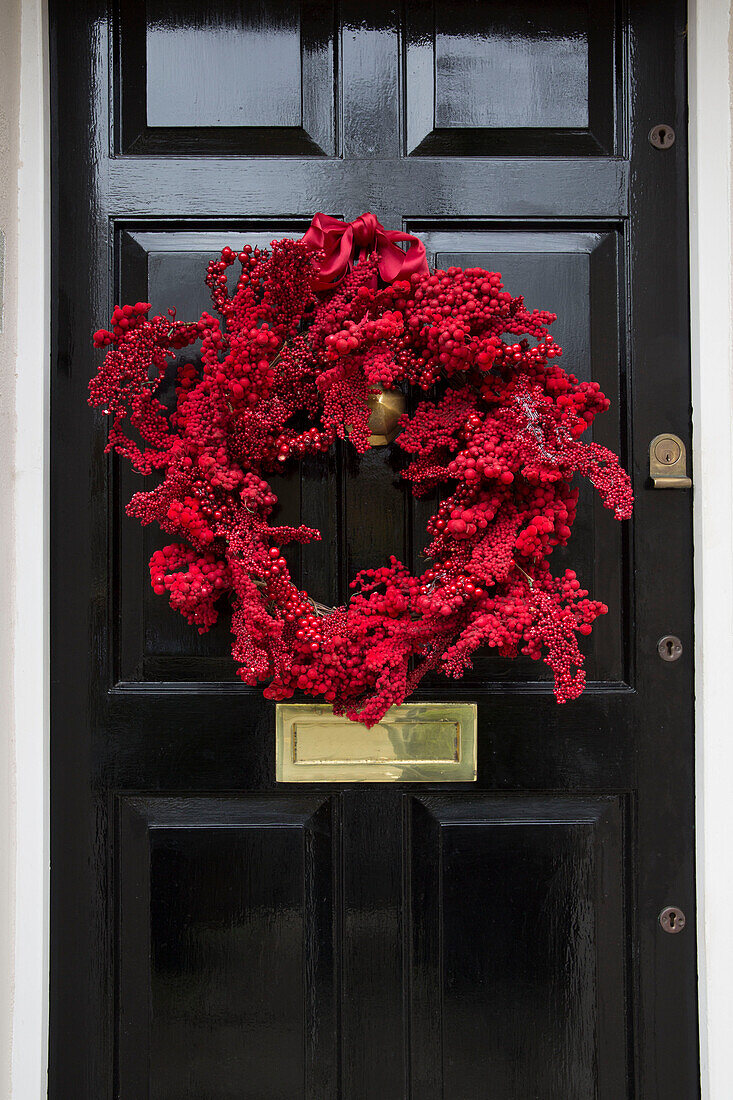 Red berry wreath on black front door of London townhouse UK