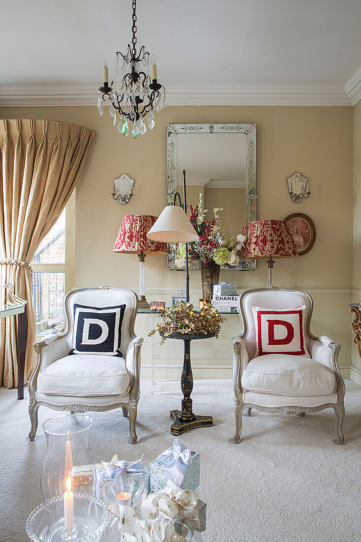 Pair of upholstered armchairs with letter D cushions below chandelier in London townhouse UK