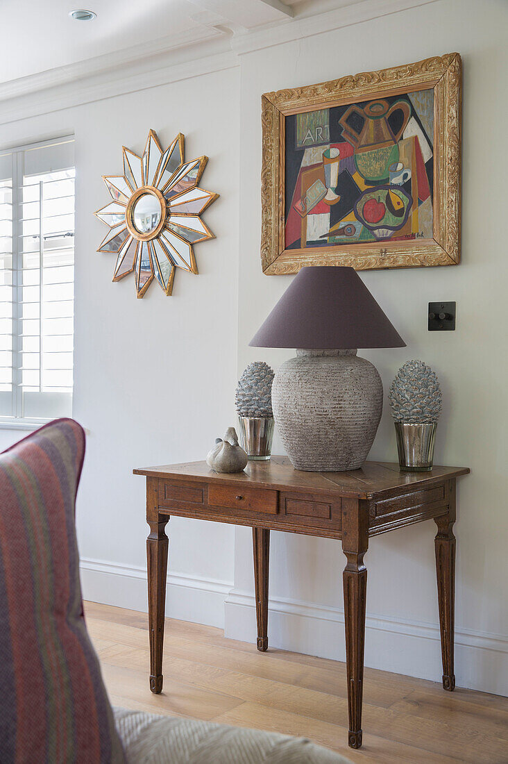 Lampe und Ornamente auf Holztisch mit Kunstwerk und Spiegel in einem Haus in West Sussex