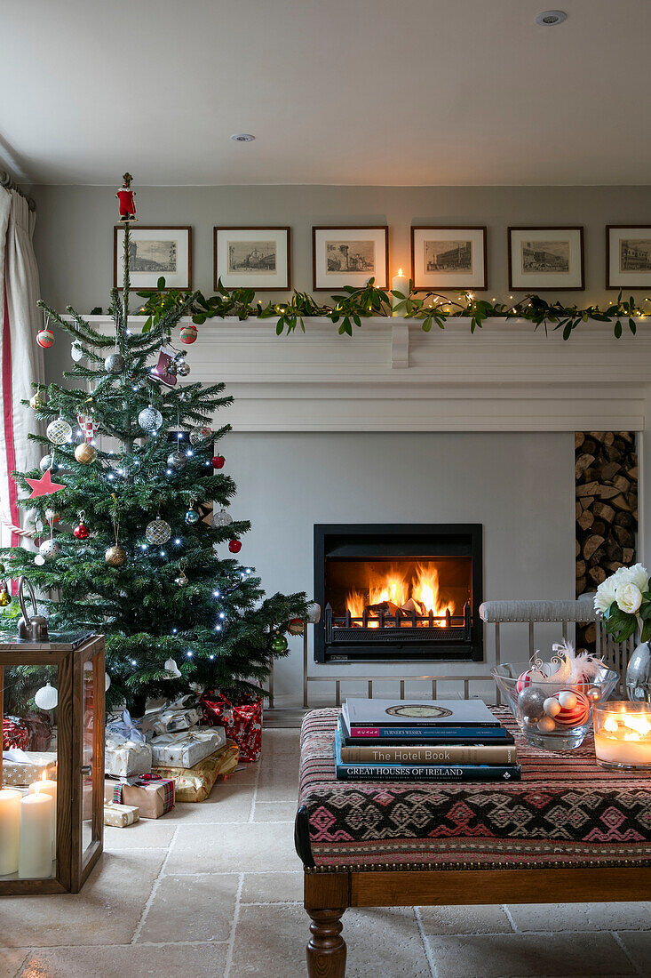Christmas tree with presents and lit fire in living room of Dorset farmhouse UK