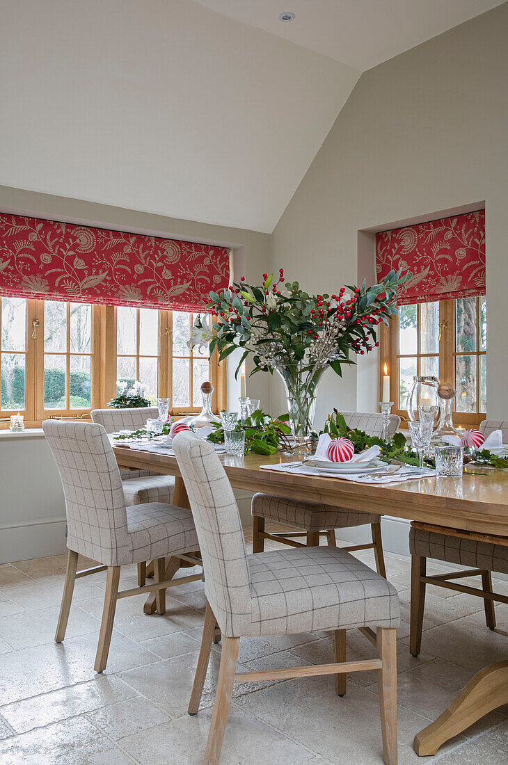 Checked dining chairs at table with red foliate blinds at windows in Dorset farmhouse UK
