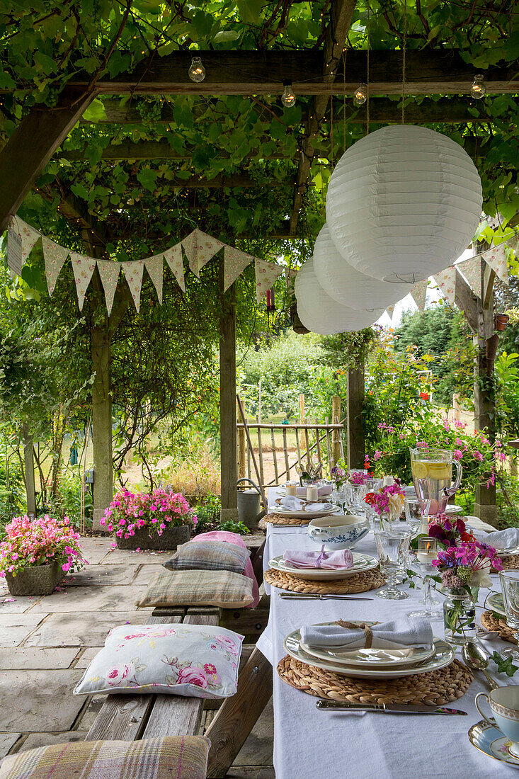 Papierschirme hängen an einer Pergola über einem Esstisch mit Sitzkissen und Wimpeln im Garten von Alford in Surrey, Großbritannien