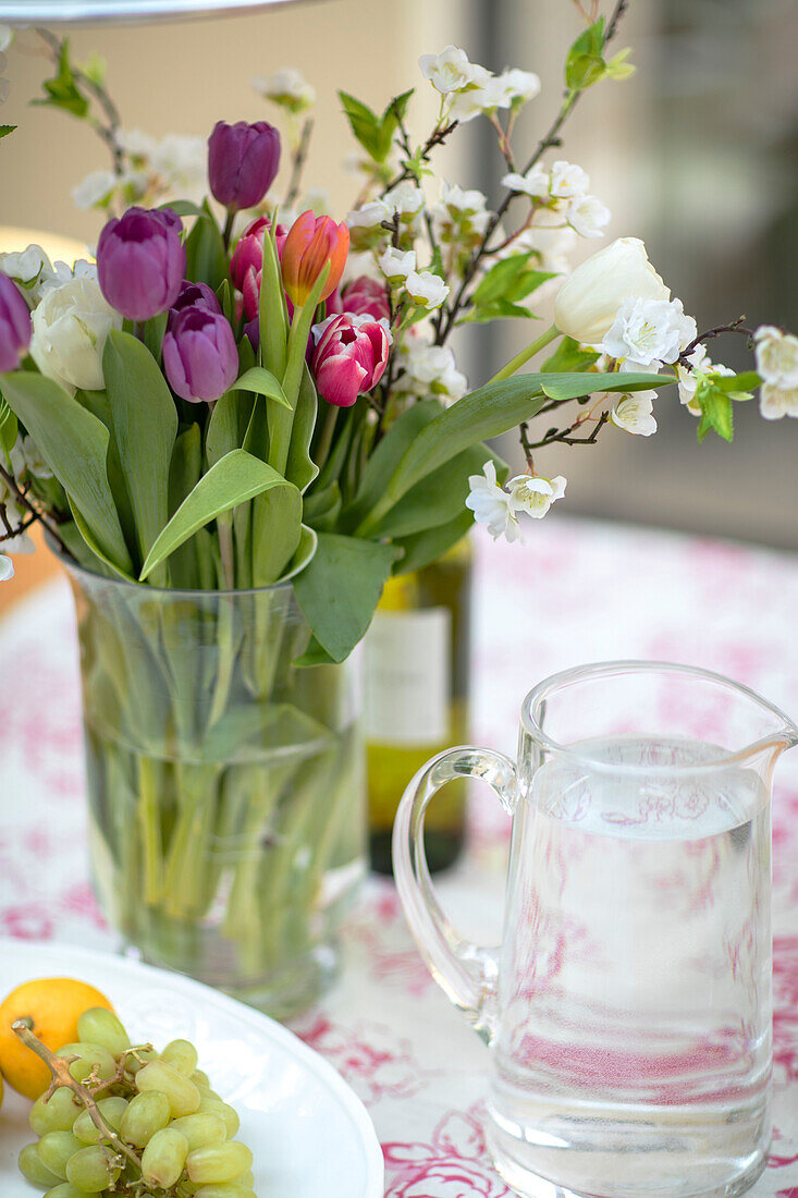 Vase mit Frühlingsblumen und Obst auf einem Tisch in einer umgebauten Scheune in Gloucestershire UK