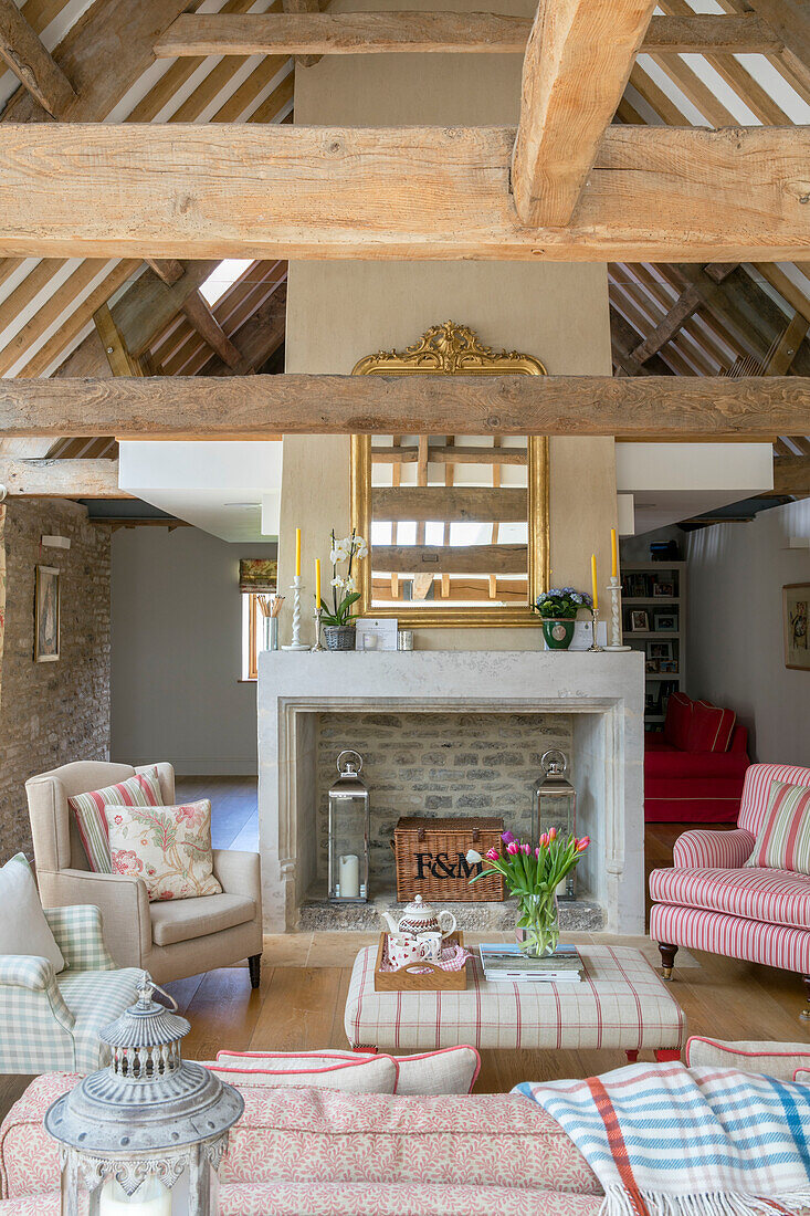 Gilt framed mirror above fireplace with armchairs in beamed living room of Gloucestershire barn conversion UK