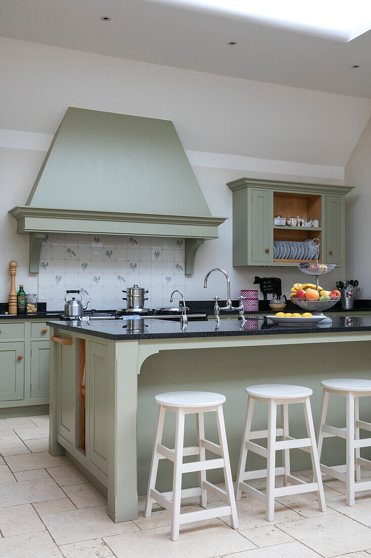 Weiße Hocker an der Frühstücksbar in einer Küche mit hellgrünem Dunstabzug in einer umgebauten Scheune in Gloucestershire UK