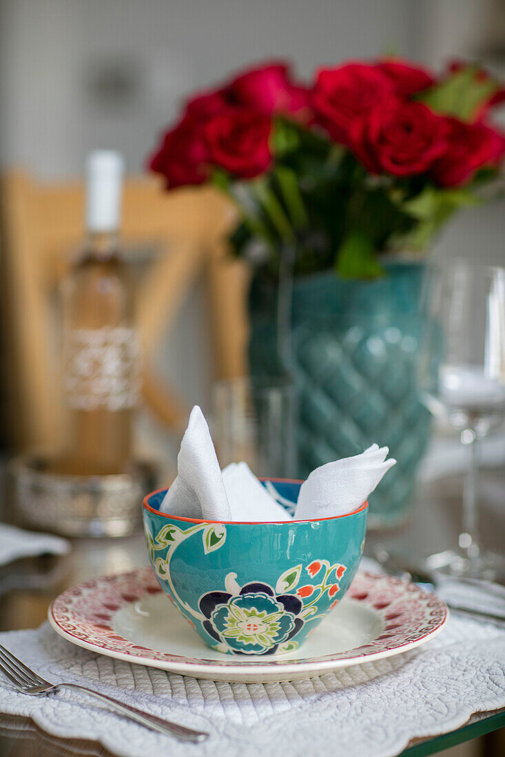 Napkin in turquoise ceramic bowl with red roses in London home UK