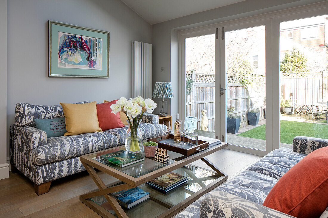 Grey sofas with wooden glass topped coffee table and view to garden in London home UK