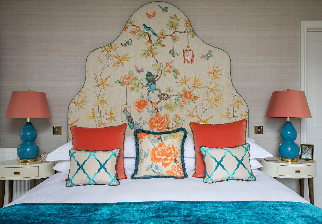 Embroidered headboard with orange cushions an turquoise blanket and lamps in 1950s style Wiltshire bedroom