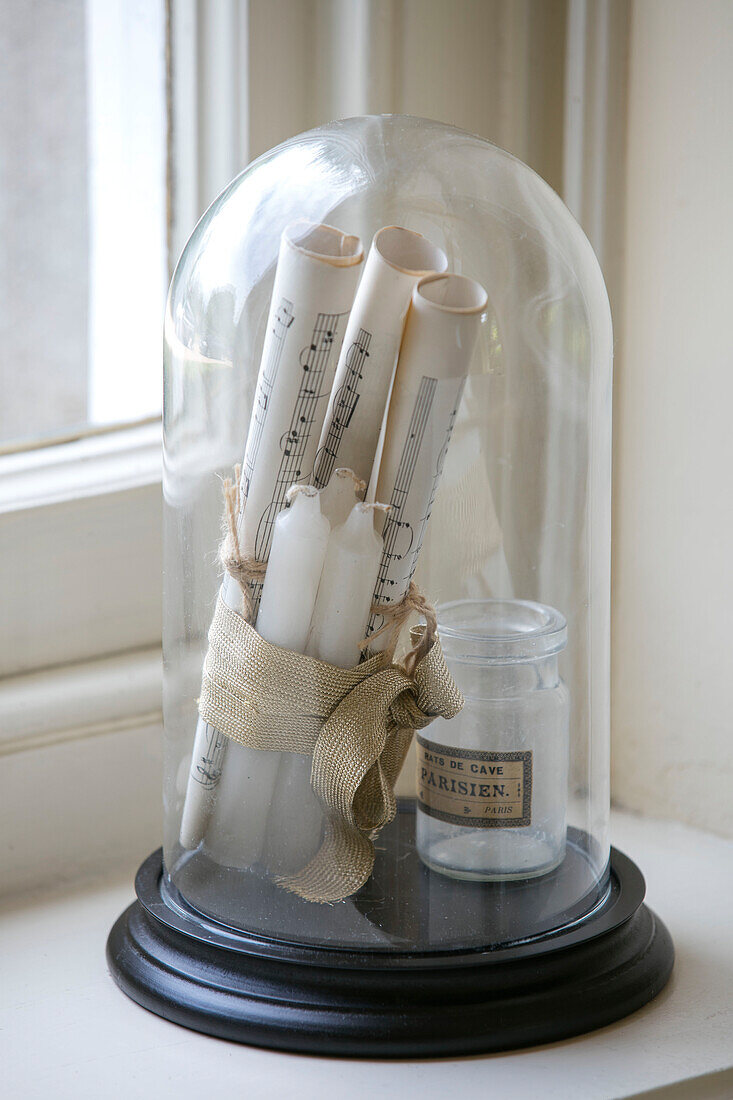 Rolled sheet music and candles tied with gold ribbon under bell jar in detached Kent home UK