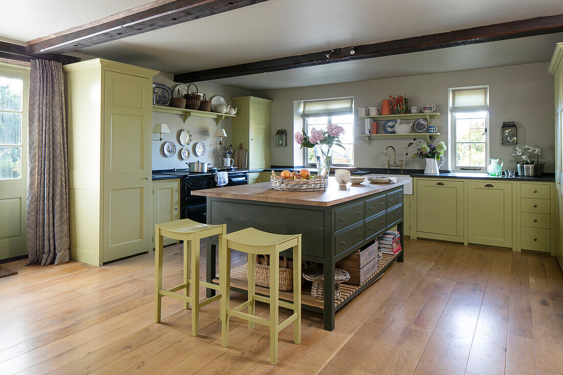 Gelbe Barhocker an grüner Kücheninsel in einem geräumigen Haus in Somerset, Großbritannien