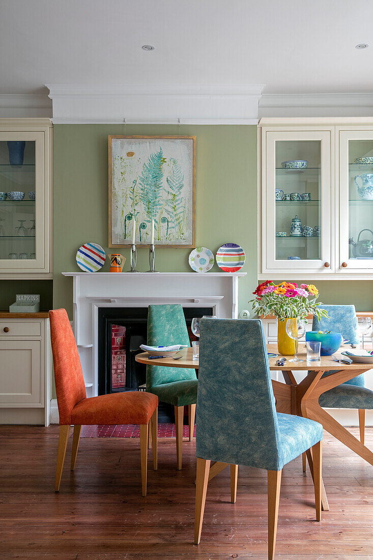 Verschiedene Stühle am Tisch in einem hellgrünen Esszimmer mit Glasvitrinen in einem Haus im Arts and Crafts-Stil in Sevenoaks, Kent, Großbritannien