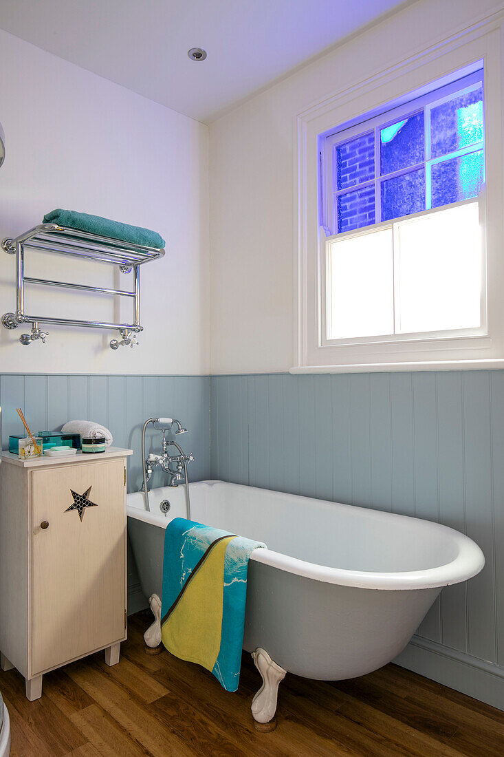 Freistehende Badewanne unter dem Fenster mit hellblauer Nut- und Federverkleidung in einem Reihenhaus in Sevenoaks, Kent UK