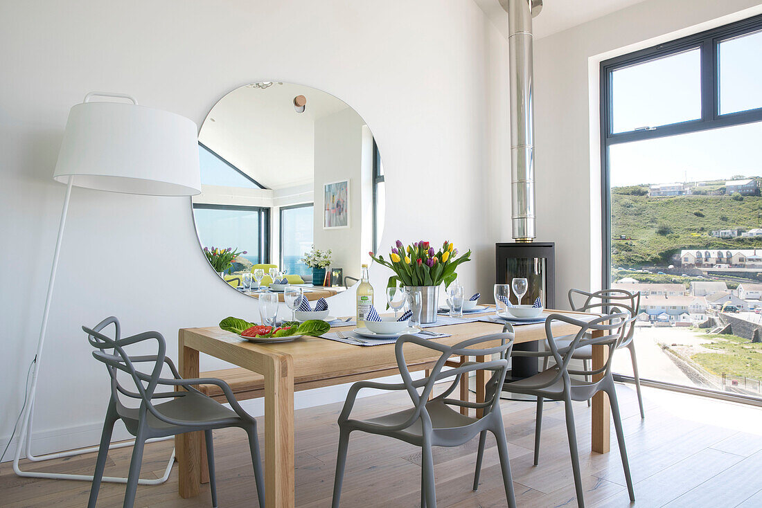Graue Esszimmerstühle am Tisch mit großer Lampe und Spiegel im Neubau Cornwall UK