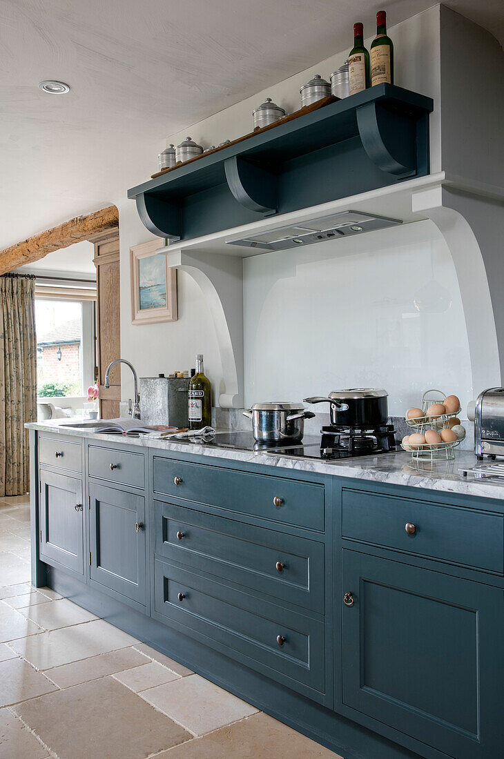 Pans on hob below shelf in teal fitted kitchen in Oxfordshire home UK