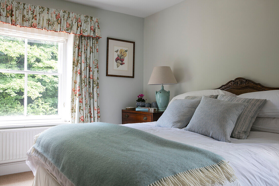 Hellgrüne Decke auf einem Doppelbett mit geblümten Vorhängen in einem Haus in Hampshire, UK