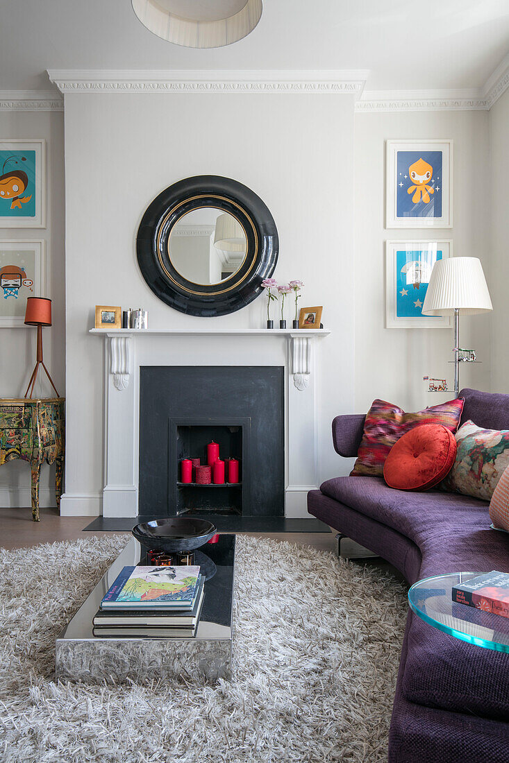 Curved purple sofa with low table and circular mirror above fireplace in North London home UK