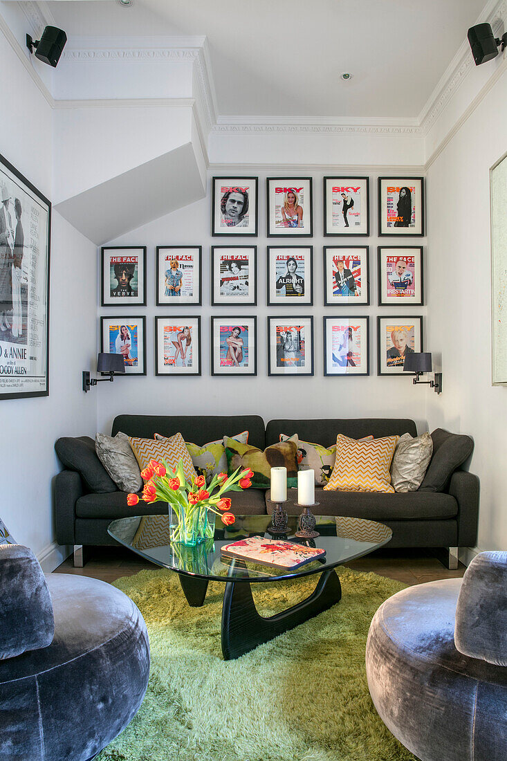 Bilderwand mit Postern über einem grauen Sofa und einem Couchtisch mit Glasplatte in einem Haus im Norden Londons UK
