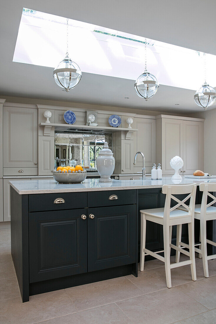 White bar stools at grey kitchen island under skylight with glass pendants in Sussex home UK