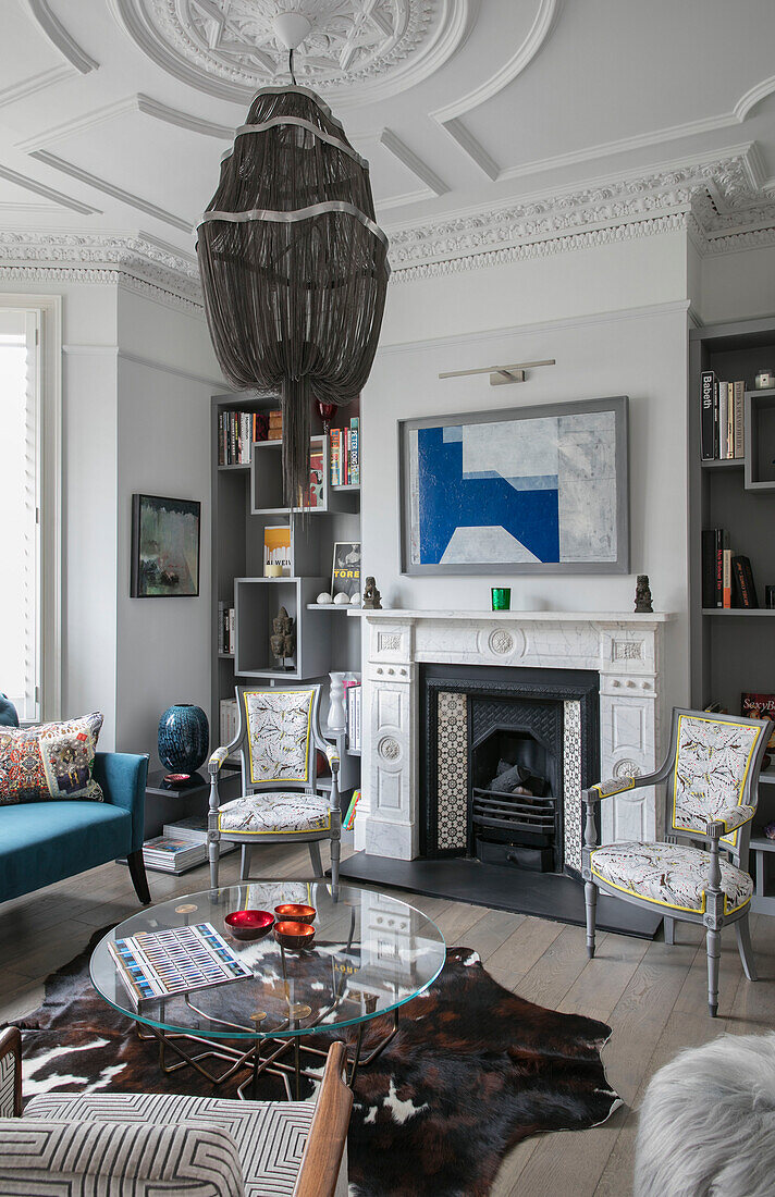 Modern art above fire with animal skin rug and large pendant in London home UK