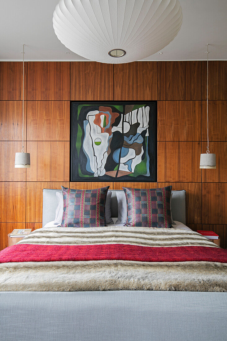 Modern art above double bed with cushions and wood panelling in London home UK