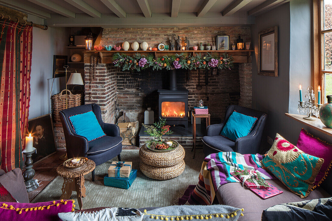 Paar graue Sessel mit beleuchtetem Feuer und farbenfrohen Textilien zu Weihnachten in einem Landhaus in Norfolk England UK