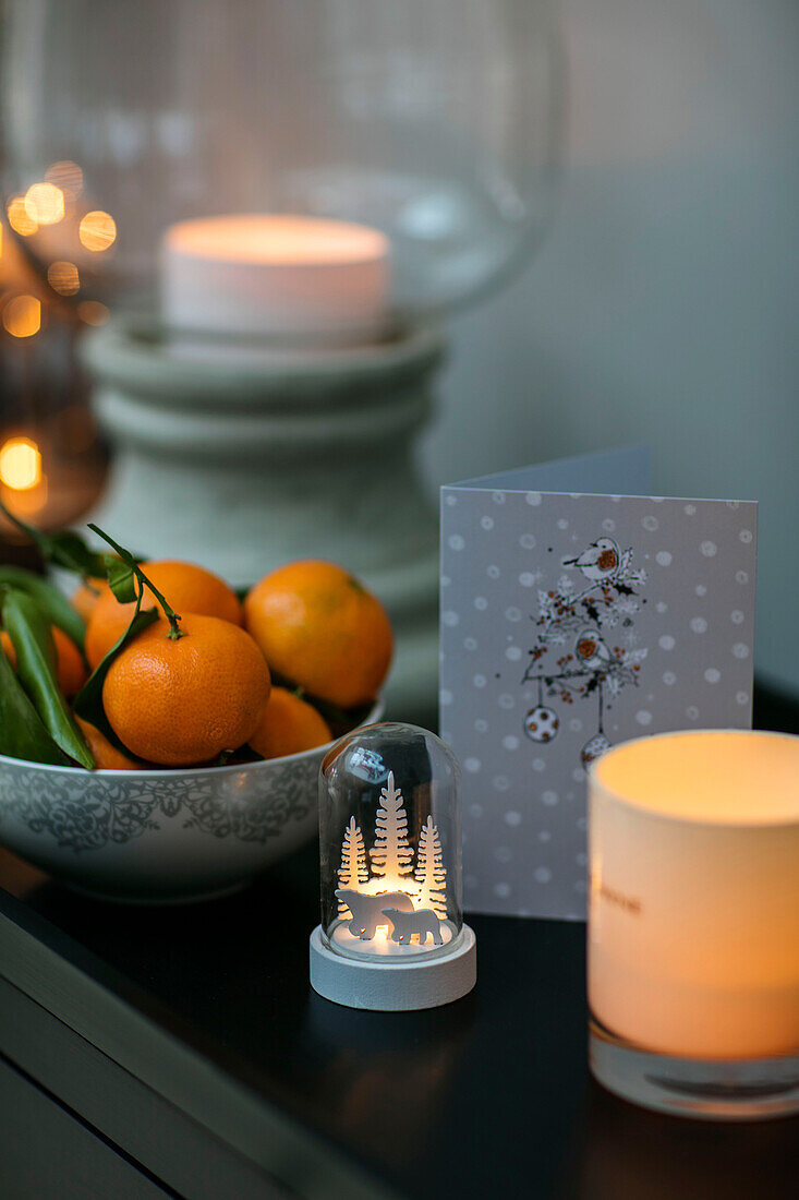 Schale mit Satsumas und brennenden Kerzen mit Weihnachtskarte in einem Haus in Hampshire UK