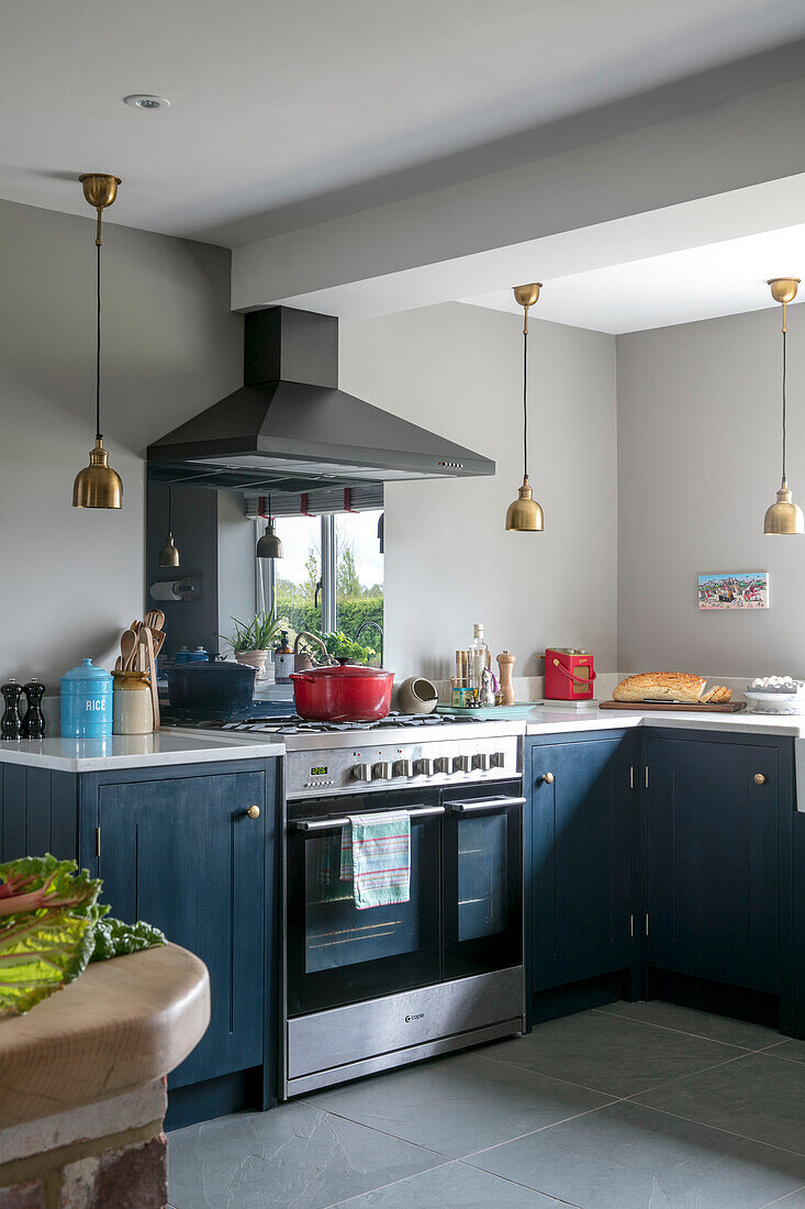 Gold pendant lights in kitchen with teal units Hampshire England UK