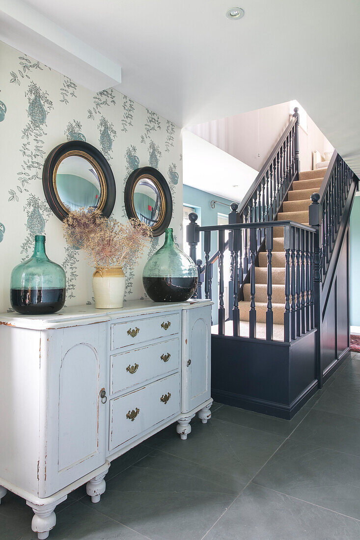 Mirrors above sideboard with black banisters in entrance hallway of Hampshire home England UK