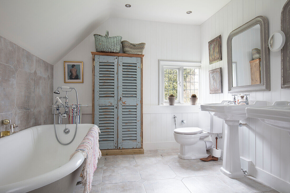 Cupboard made from salvaged shutters with freestanding bath and pedestal basins in Surrey farmhouse UK