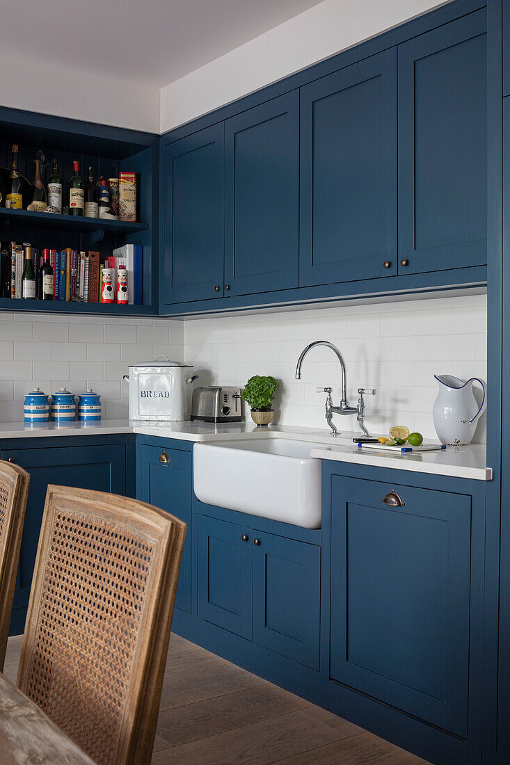 Belfast sink with bottles on shelving and blue paintwork in kitchen of North London apartment UK