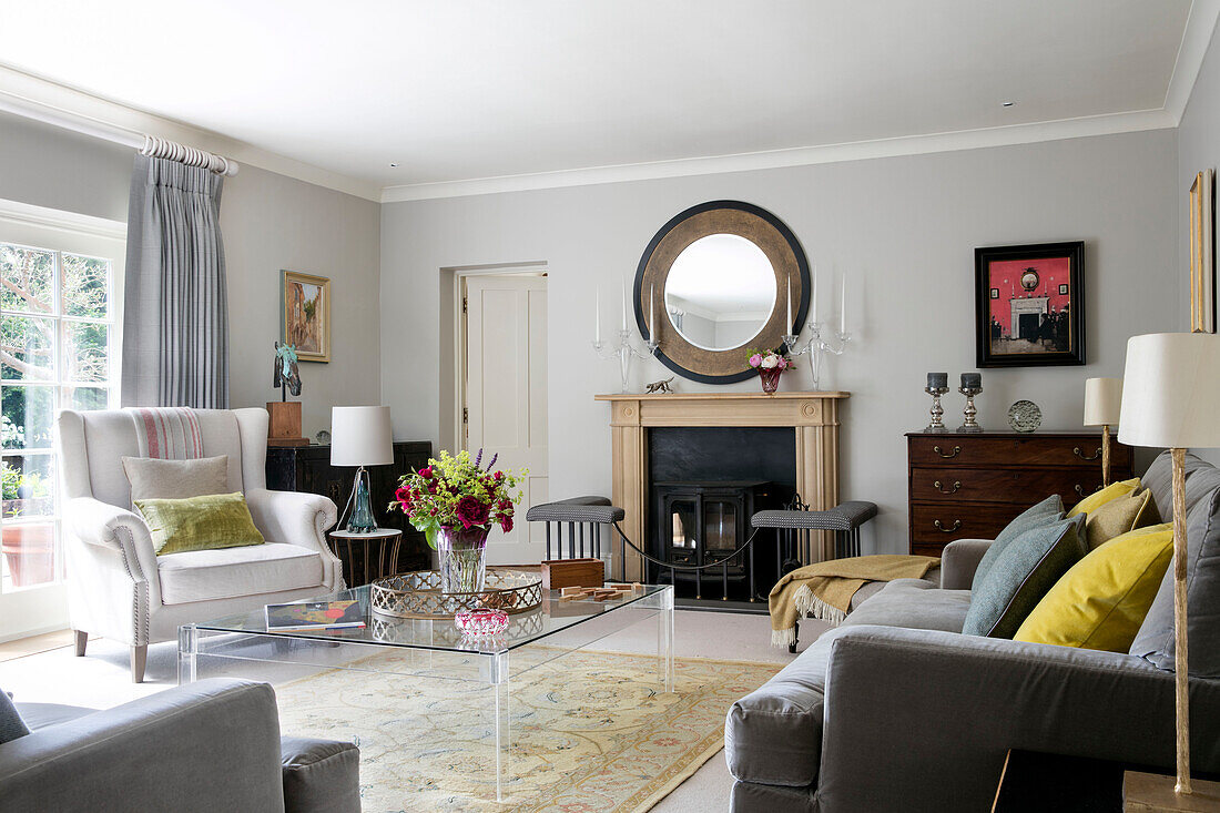 Large mirror above fireplace with glass coffee table and white armchair in living room of Victorian coach house West Sussex UK