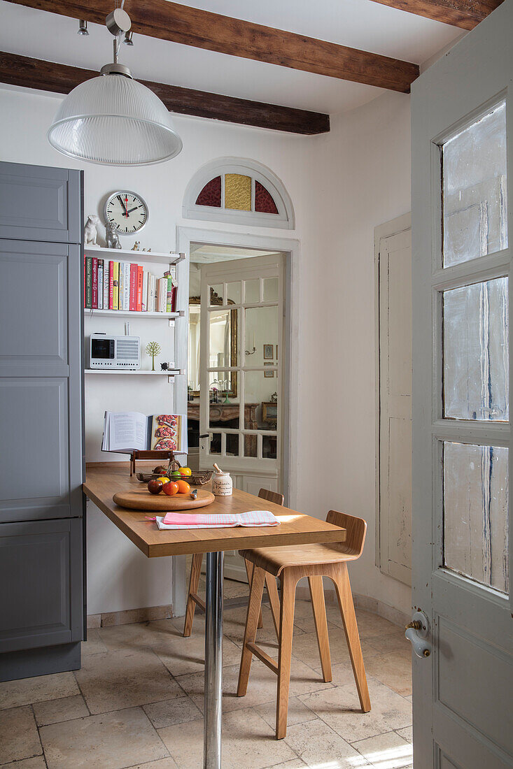 Small table and stools with grey cupboard and shelves in Issigeac kitchen Perigord France