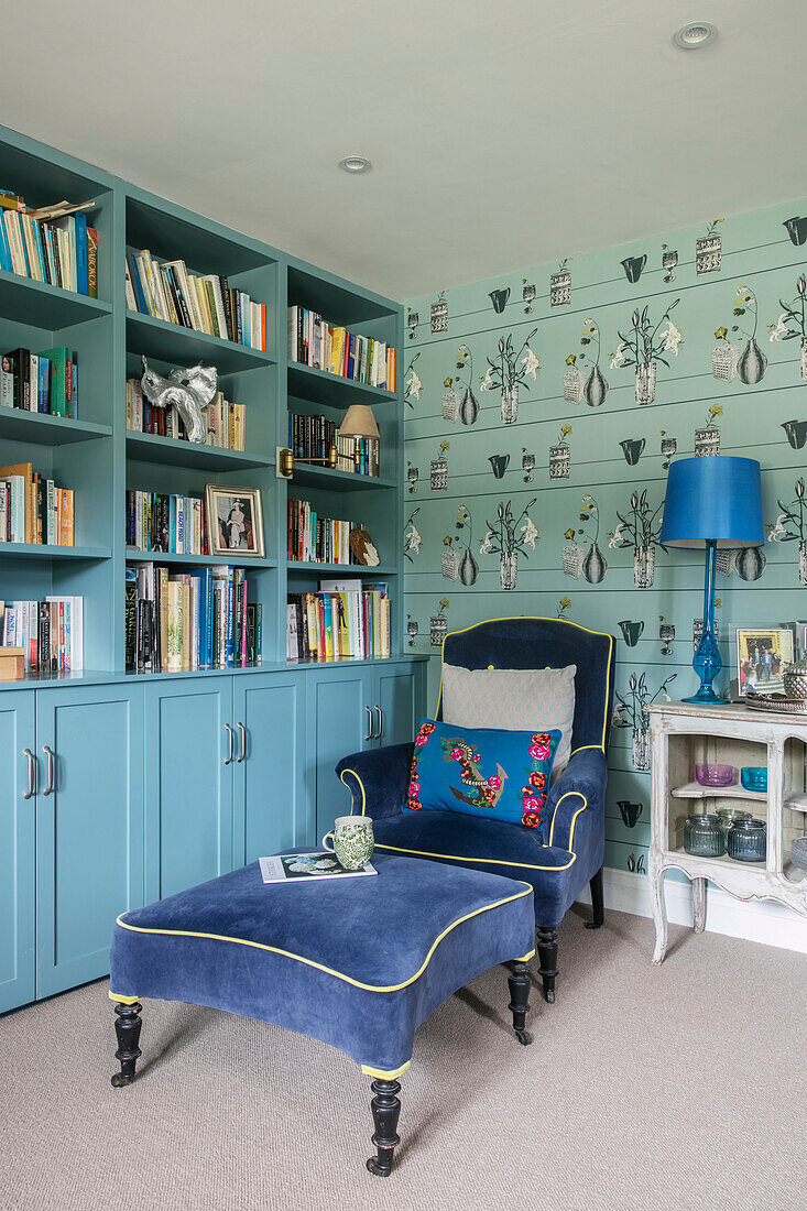 Blauer Samtsessel und Fußhocker mit türkisfarbenem Bücherregal in einem Haus in Hampshire, England UK