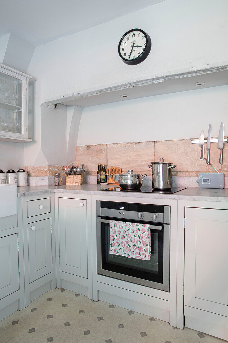 Uhr über dem Ofen mit Pfannen auf dem Kochfeld und Wänden in Pavilion Grey in einer Küche in Wiltshire UK