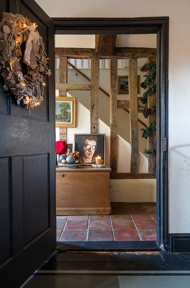Door in Off Black with Christmas wreath and terracotta tiles in timber framed hallway of Norfolk farmhouse UK