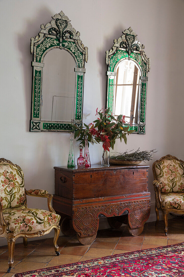 Italian mirrors above wooden chest with pair of antique chairs in French chateau Lot et Garonne