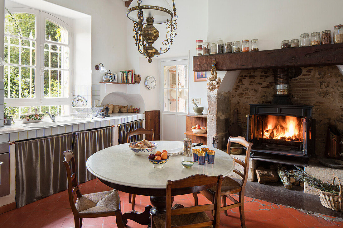 Marble topped table with early 1900s terracotta floor tiles in kitchen with lit fire in French chateau Lot et Garonne