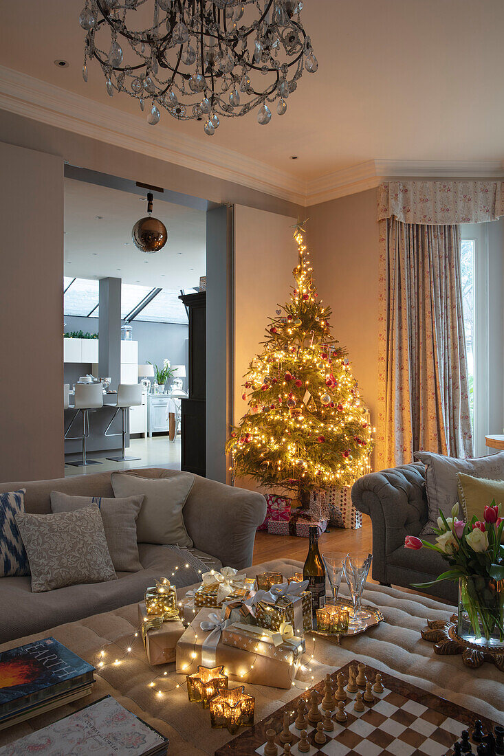 Lit Christmas tree and presents with view to kitchen in London home UK
