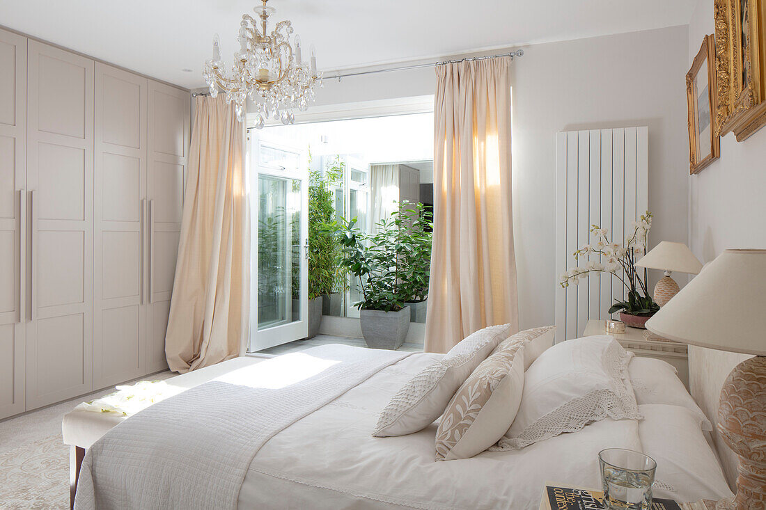Sunlit bedroom with fitted wardrobe and doors opening to balcony exterior in Victorian home London UK