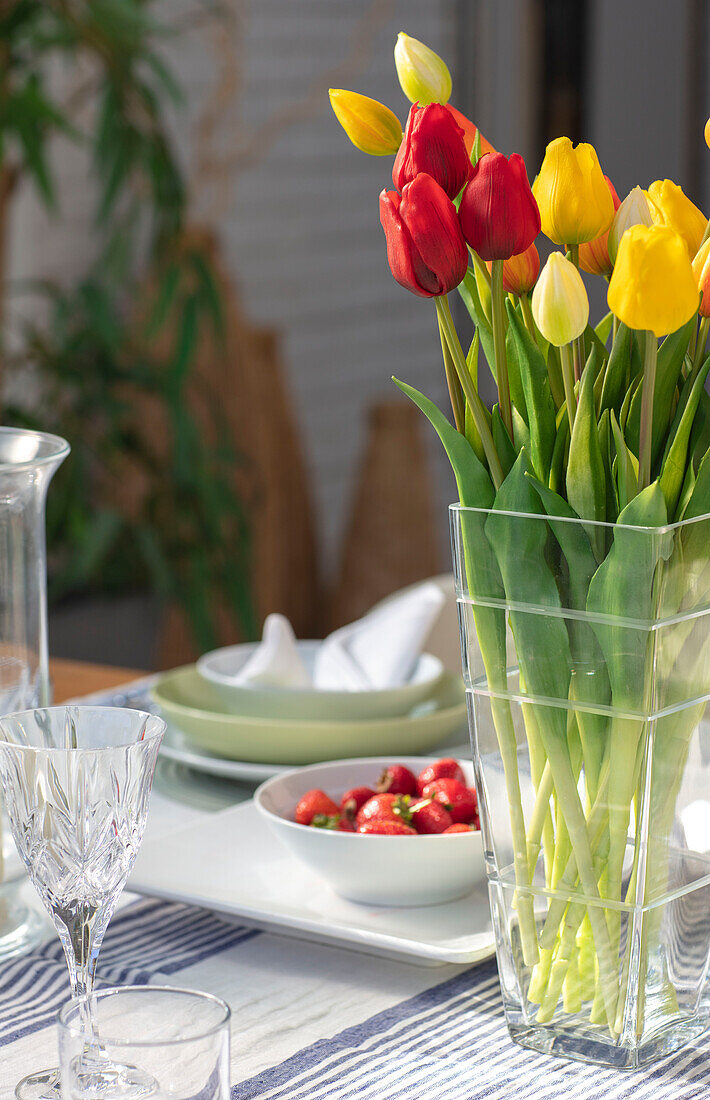 Rote und gelbe Tulpen in einer Glasvase mit Erdbeeren auf einem Tisch in einem Londoner Haus UK