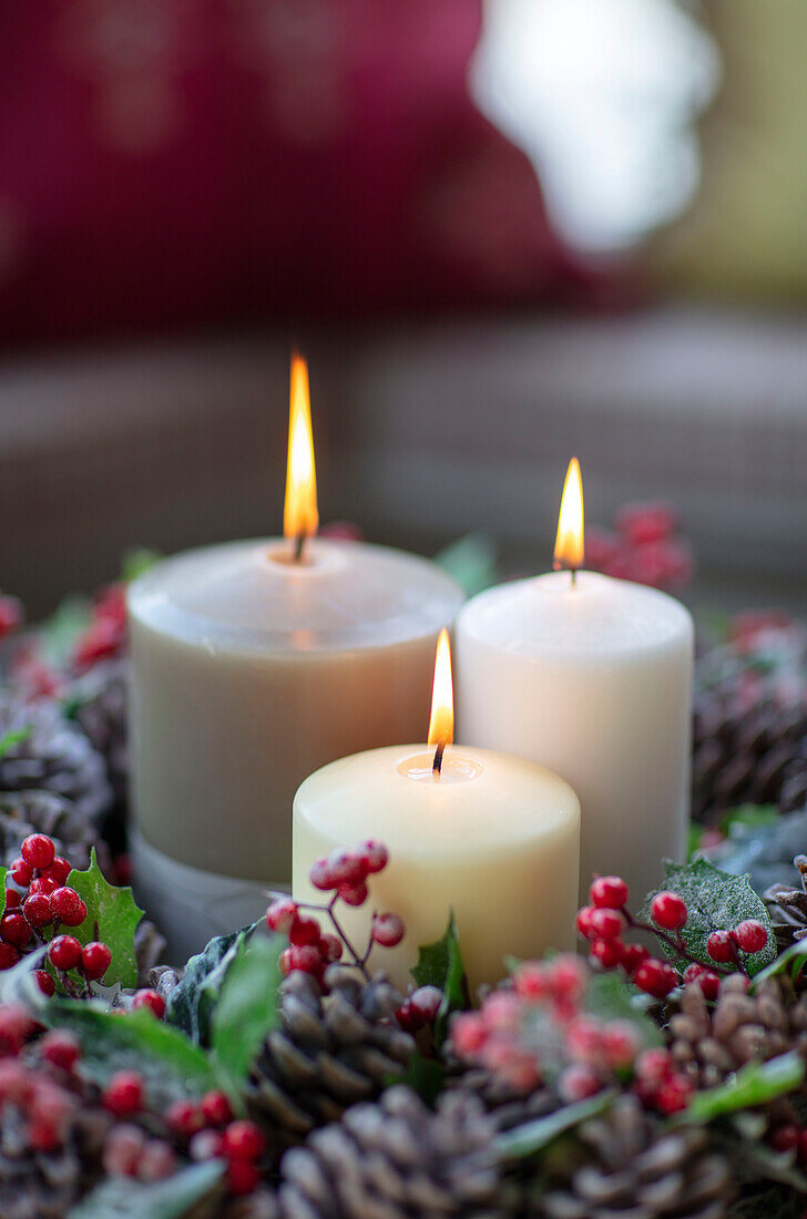 Drei brennende Kerzen in einer Girlande aus Tannenzapfen und Beeren, Hampshire, UK