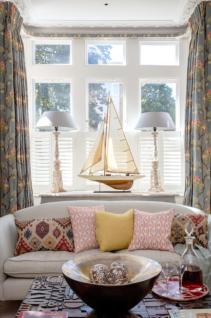 Model boat and mismatched fabrics in bay window of Southwest London home UK